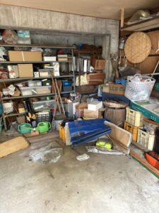 片付け前のガレージの写真。床の端や棚に様々な物が多数置かれている。