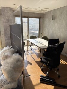 片付け前のオフィス。パーテーション、ゴミ袋、机、複数の事務椅子が置かれている。