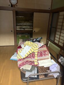 残置物撤去前　押し入れの中とベッドの上に布団や衣類が積まれている