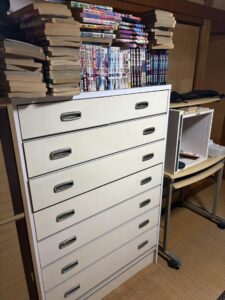 残置物撤去前　幅広のチェストの上に古い漫画が積まれている。