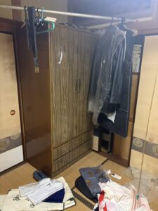 残置物撤去前　箪笥が置かれ、服がハンガーにかかっている。畳の上には衣類がいくつか置かれている。