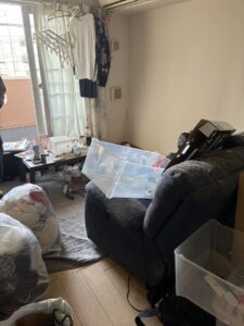 残置物撤去前の部屋。衣類が袋に詰められ、こたつの上には調味料や飲料が置かれている。