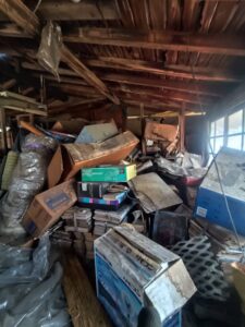 片付け前の屋根裏。段ボールや古道具、雑品が天井まで積み重ねられている