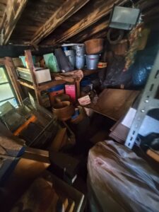 片付け前の古い物置。不用品や生活雑貨が乱雑に積み上げられている