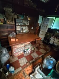古い木造住宅の台所。食器棚や冷蔵庫、家具などの生活用品が残されている。