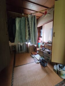 片付け前の和室。衣類が干されており、床には生活用品が置かれている。