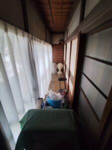 片付け前の廊下。古い家具やゴミ袋が置かれており動線が塞がっている。