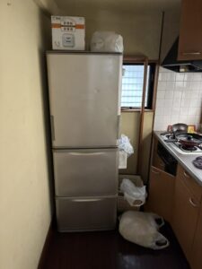 作業前のキッチン。3ドア冷蔵庫の上に箱と袋が置かれている。冷蔵庫の横にもレジ袋が散乱している。