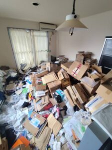 1Rの居室　残置物撤去前。天井にも迫りそうなほど段ボールなどが積まれており、床が物で埋められている。