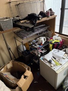 作業前の室内。解体されたメタルラックや布製品や文具が乱雑に置かれている。