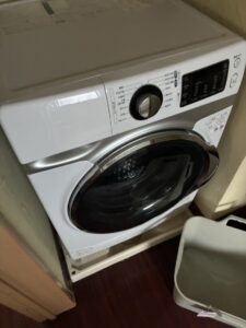 作業前の脱衣所のドラム式洗濯機。足元に洗濯カゴが置かれている。